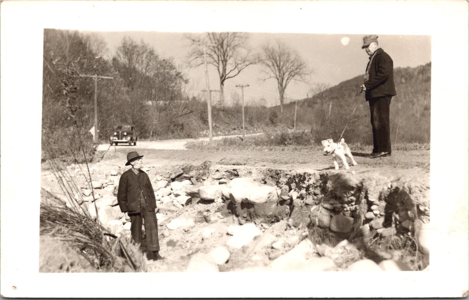 RPPC POSTCARD-TWO MEN AND DOG ON SHOULDER OF ROAD