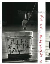 1985 Press Photo A person drop a money on The Flying Neutrinos bucket picture